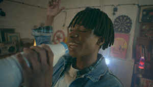 Jeune homme entrain de chanter avec une bouteille de lait en guise de micro, derrière lui une boule disco réalisé en VFX par Tronatic Studio, Paris et Tours